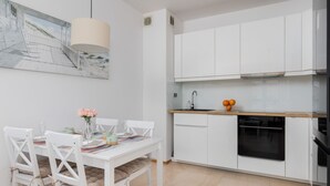 Una cocina moderna con armarios blancos, encimera de madera y una zona de comedor con sillas y una mesa blancos.
