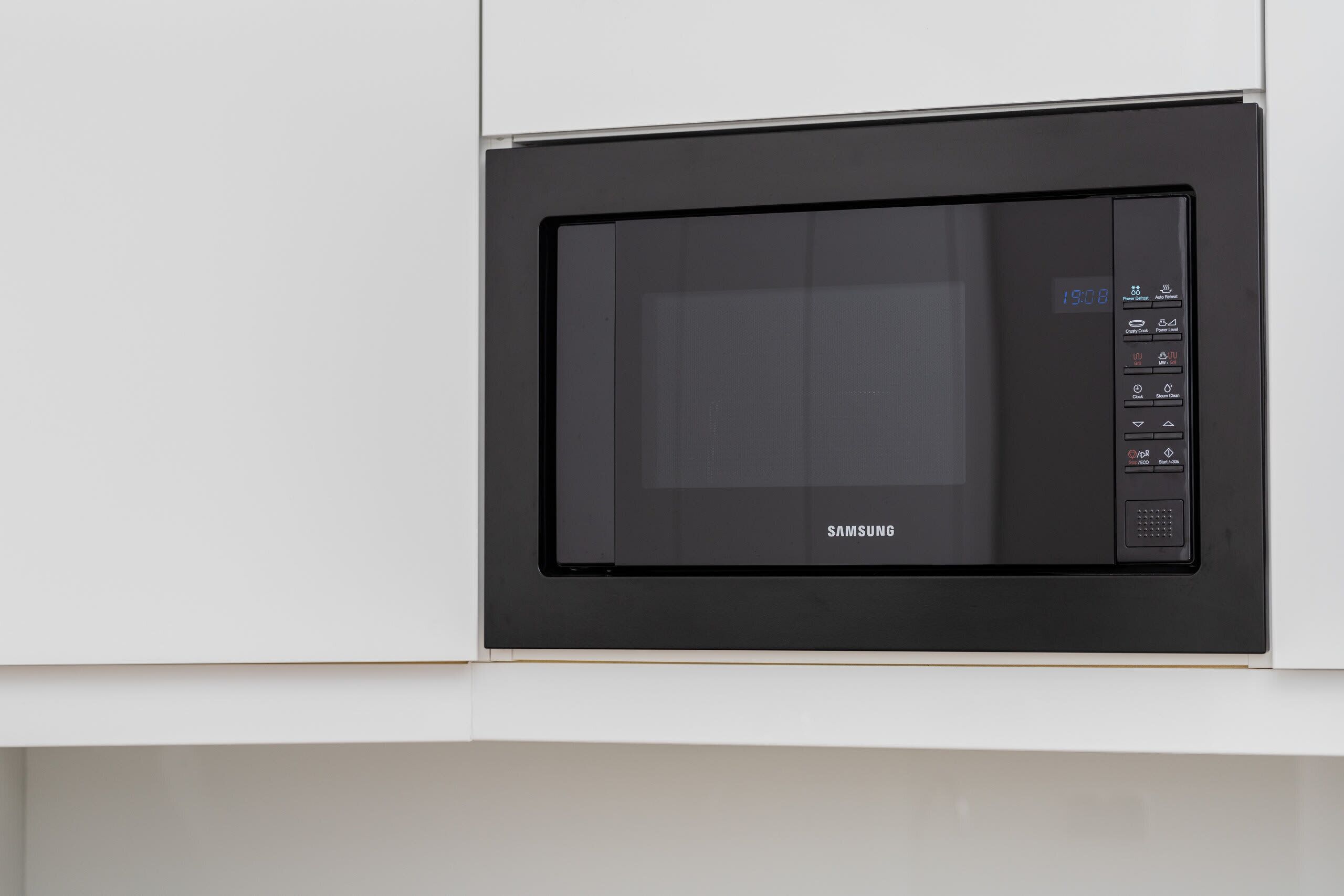 Een zwarte Samsung magnetron ingebouwd in een wit keukenkast.