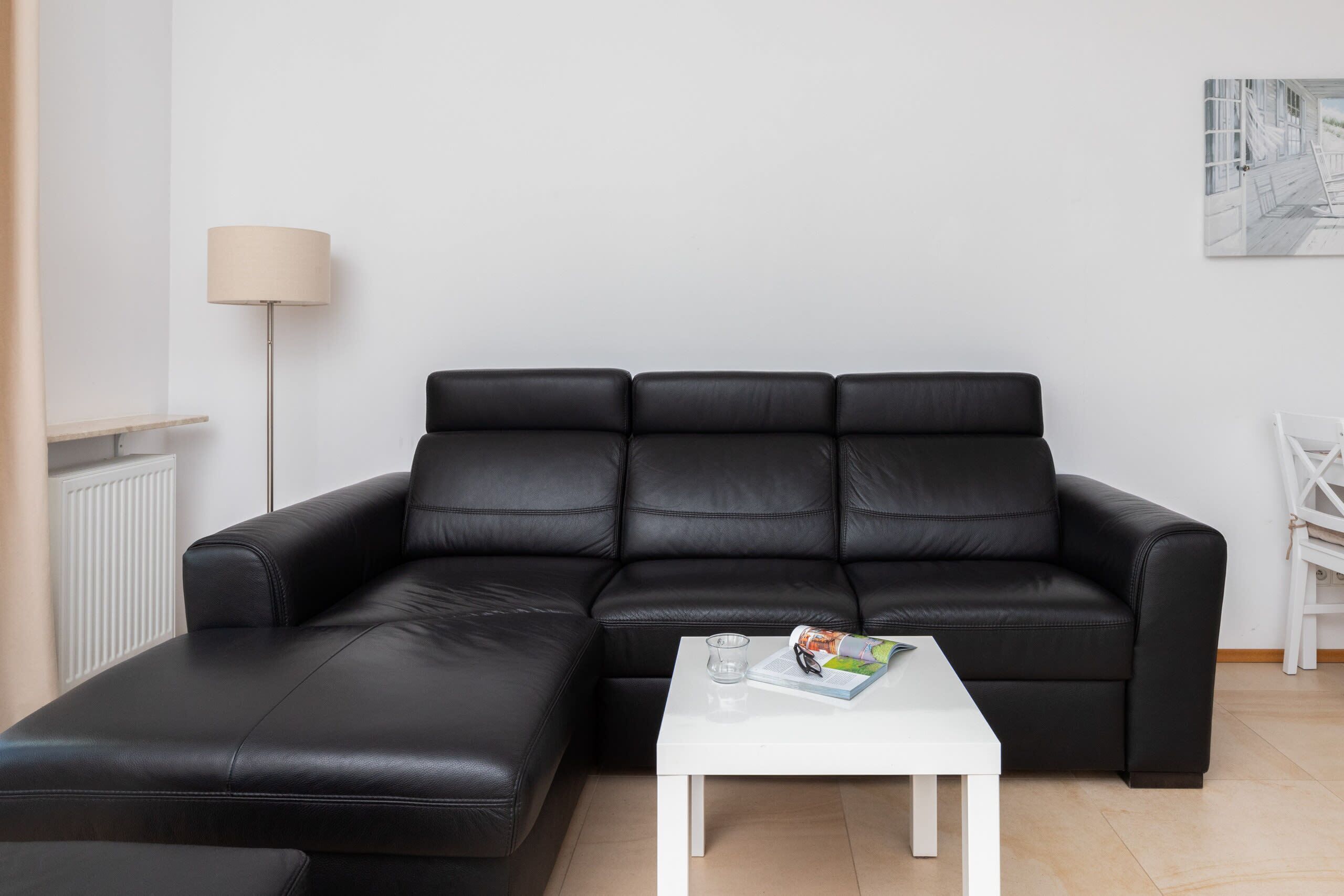Een moderne woonkamer met een zwarte leren bank, een witte salontafel en een vloerlamp.