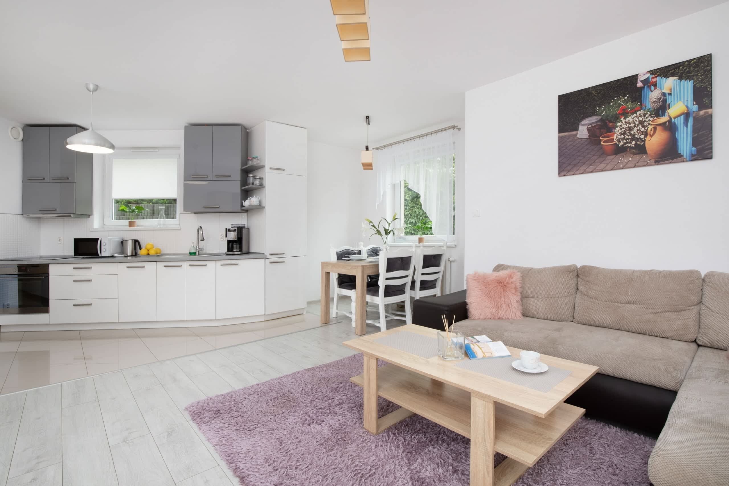 A modern kitchen with white cabinets, a dining area with a table and chairs, and a living room with a sofa and a painting on the wall.