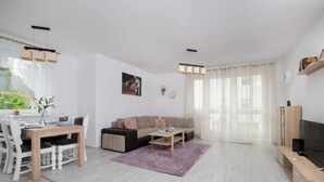Un salon moderne comprenant un coin repas, un canapé, une table basse et un téléviseur posé sur un meuble en bois.