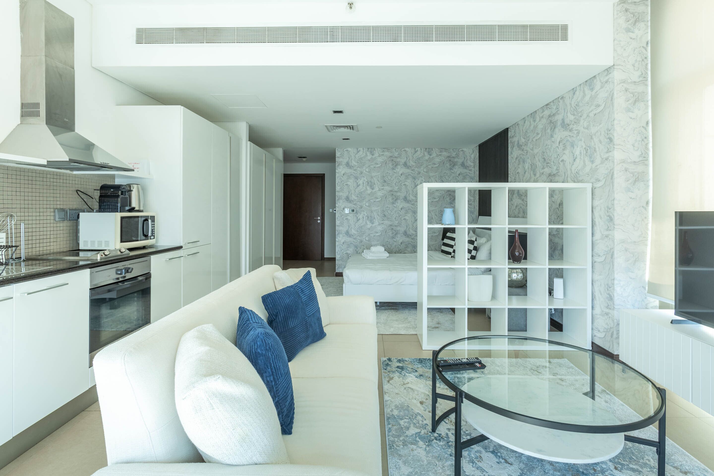 Een moderne woonkamer met een witte bank, een glazen salontafel en een witte wandplank.