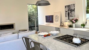Une cuisine moderne dotée d’un plan de travail en marbre, d’une cuisinière à gaz et d’une bouilloire blanche. On y trouve également un coin repas avec un canapé blanc et une chaise en métal.