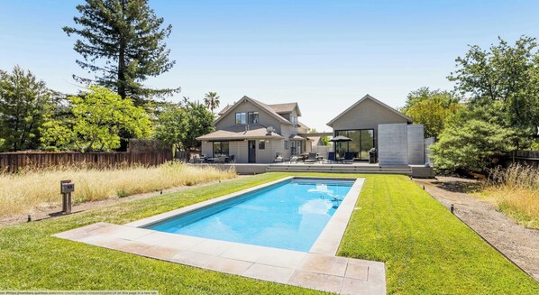 A modern two-story house with a swimming pool, a patio with outdoor furniture, and a fenced yard.