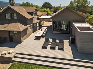 A modern residential complex with multiple houses, a shared deck area with outdoor seating, and a large glass window.