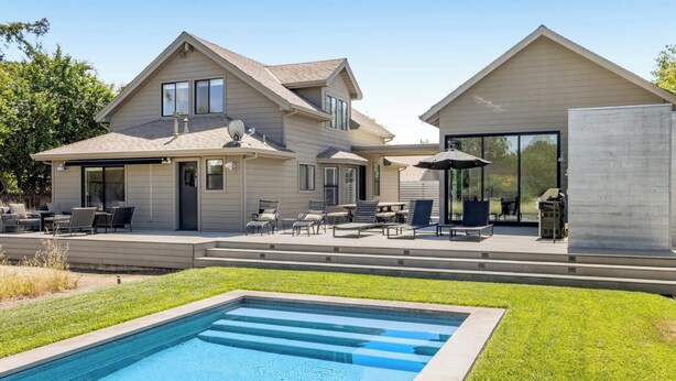 Une maison à deux étages avec une piscine, un espace salon extérieur et une grande porte vitrée.