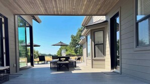 Une terrasse couverte avec une table et des chaises, de grandes fenêtres et une vue sur l’extérieur.