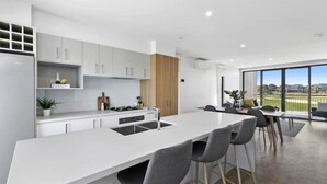 A modern kitchen with white cabinets, a central island, and a dining area with a large window offering a view of a sports field.