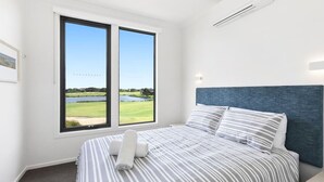 A bedroom with a bed, two windows, and a view of a golf course and lake.