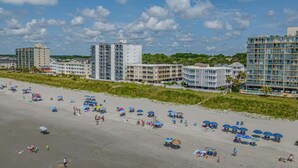 A beachfront hotel with multiple buildings, a sandy beach with umbrellas, and a clear sky. - Seafarer Unit 107 - Oceanview (North Myrtle Beach)