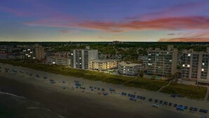 A coastal hotel with multiple buildings, a beach with umbrellas, and a sunset sky. - Seafarer Unit 107 - Oceanview (North Myrtle Beach)
