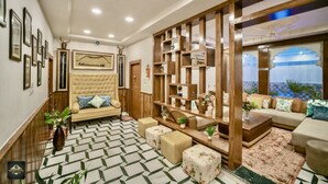 A spacious living area with a sofa, ottomans, and a wooden bookshelf. - Pax Rafahiya Haveli Udaipur (Udaipur)