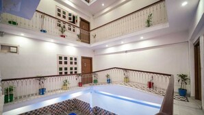 A multi-level indoor swimming pool with a checkered floor pattern, surrounded by white walls and balconies with potted plants. - Pax Rafahiya Haveli Udaipur (Udaipur)