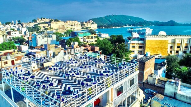 A rooftop terrace with blue patterned chairs and a view of a coastal cityscape. - Pax Rafahiya Haveli Udaipur (Udaipur)