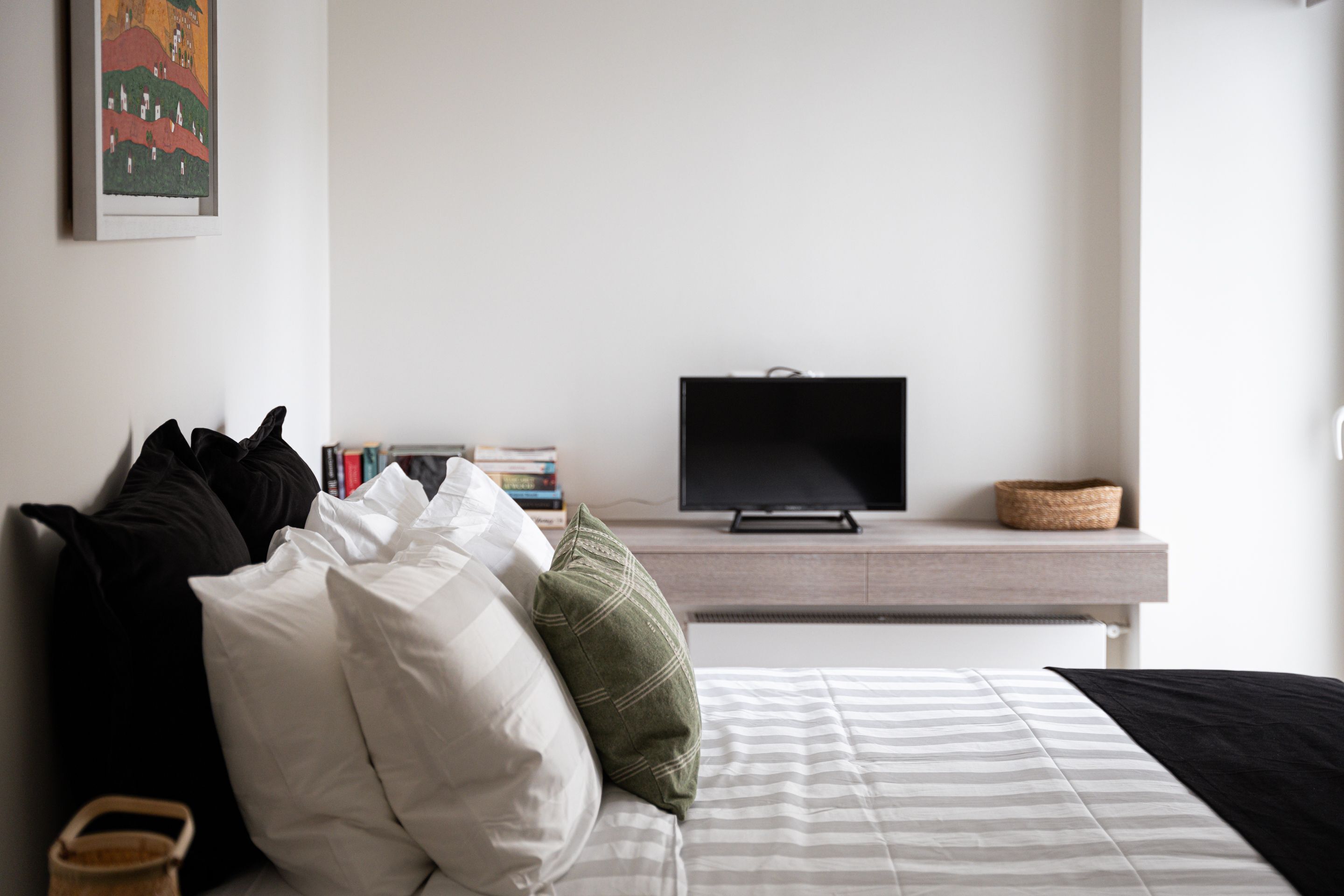 A neatly arranged bedroom with a bed, pillows, a television, and a bookshelf.