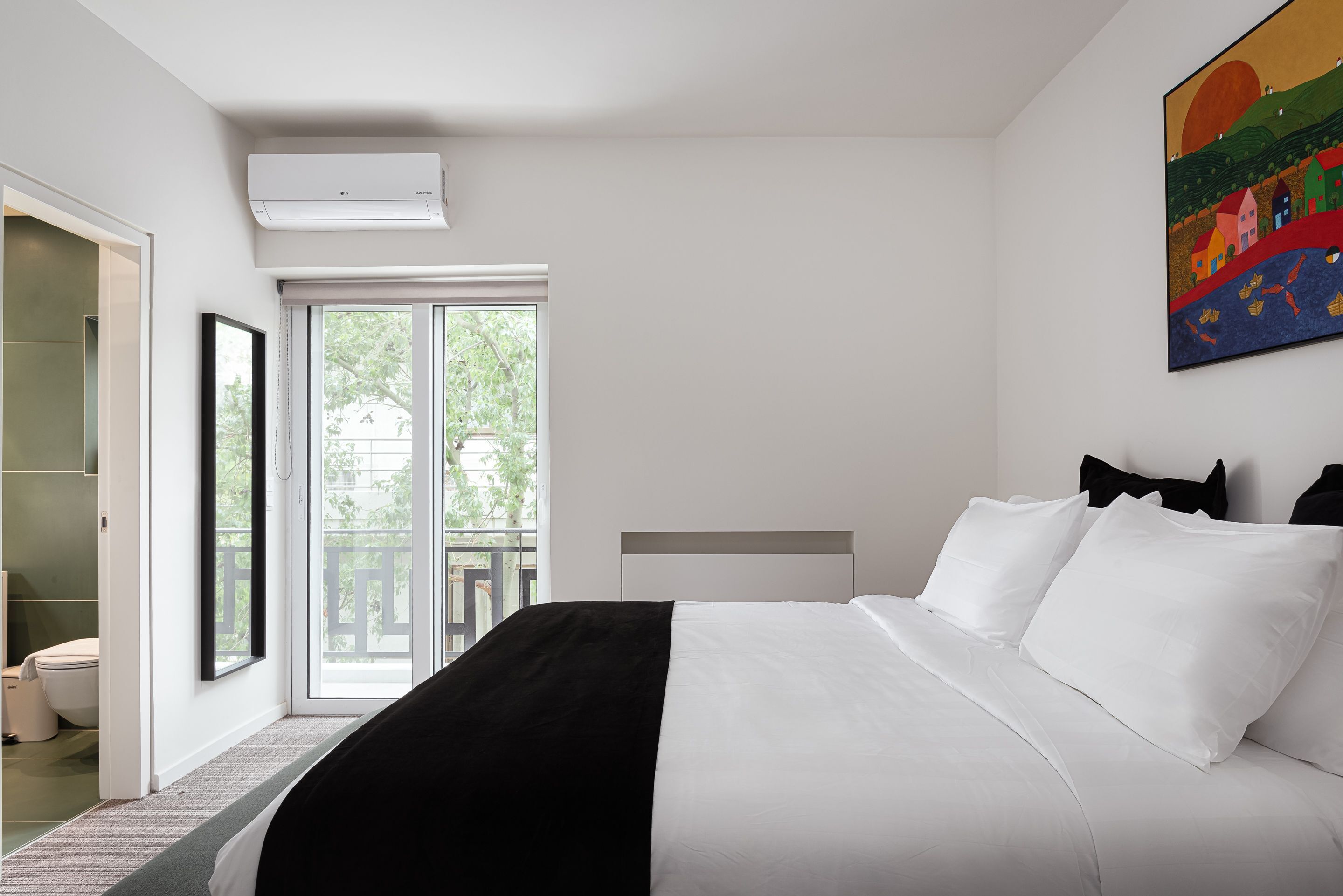 A modern hotel room with a large bed, a sliding glass door to the balcony, and a painting on the wall.