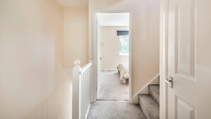 Un couloir avec un escalier recouvert de moquette menant à une chambre à coucher équipée d’un lit et d’une fenêtre.