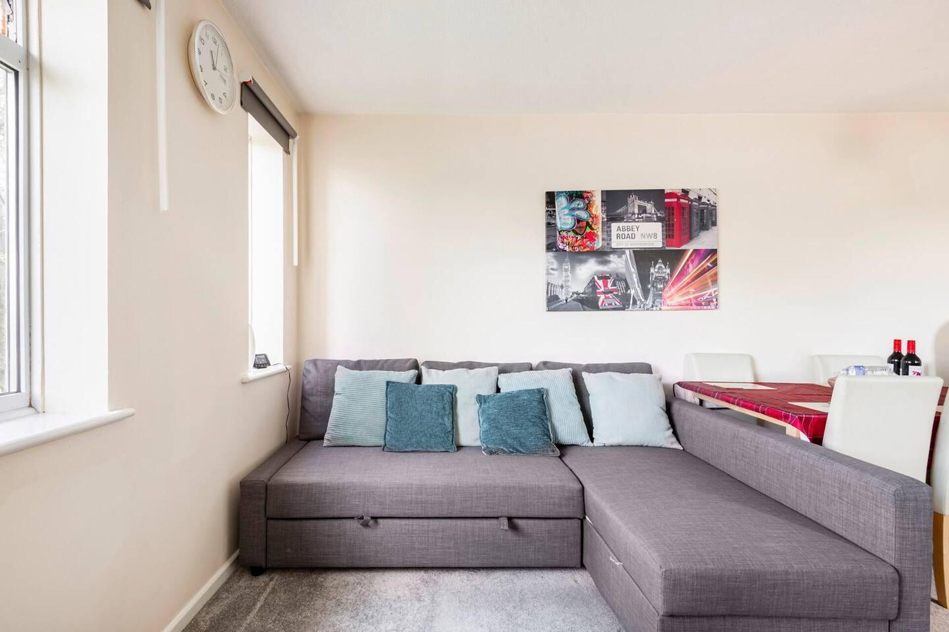 A modern living room with a grey sectional sofa, a clock on the wall, and a cityscape poster.