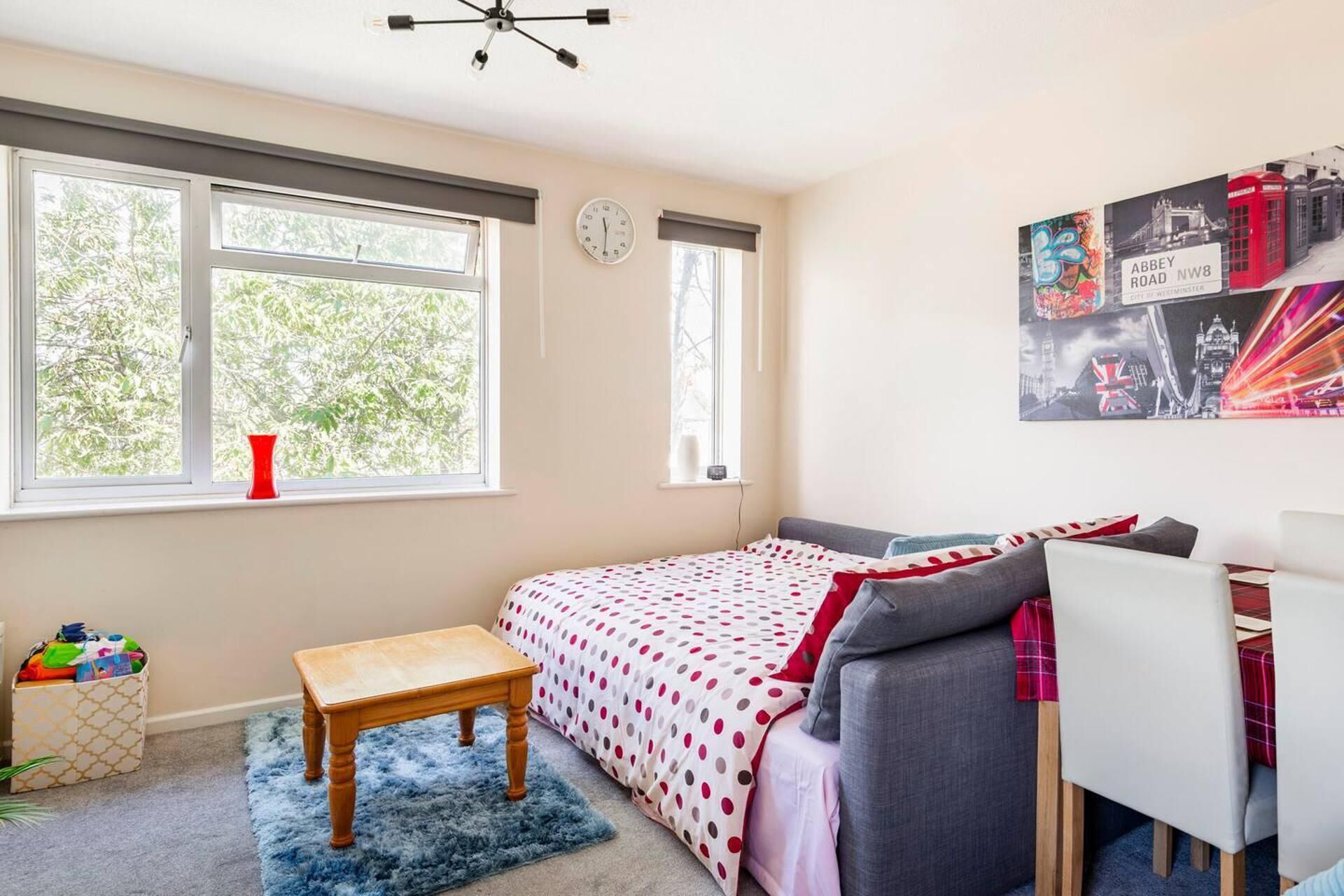Une chambre à coucher avec un lit, un bureau, une chaise, une petite table et une horloge au mur.