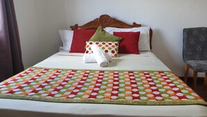 Ein ordentlich gemachtes Bett mit farbenfroher Spitze und einem hölzernen Kopfteil, daneben ein grauer Stuhl.