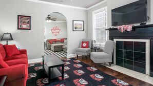 Una sala de estar con un sofá rojo, una mesa de centro negra, un tapete estampado, una chimenea y un televisor montado encima.