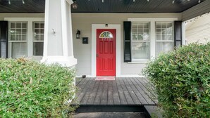 Una casa con puerta roja, columnas blancas y un porche con luces colgantes.