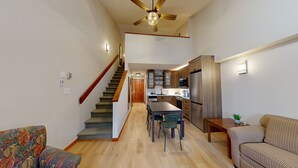 Amplia sala de estar con una escalera que conduce a una cocina, una mesa de comedor con sillas y un sofá.