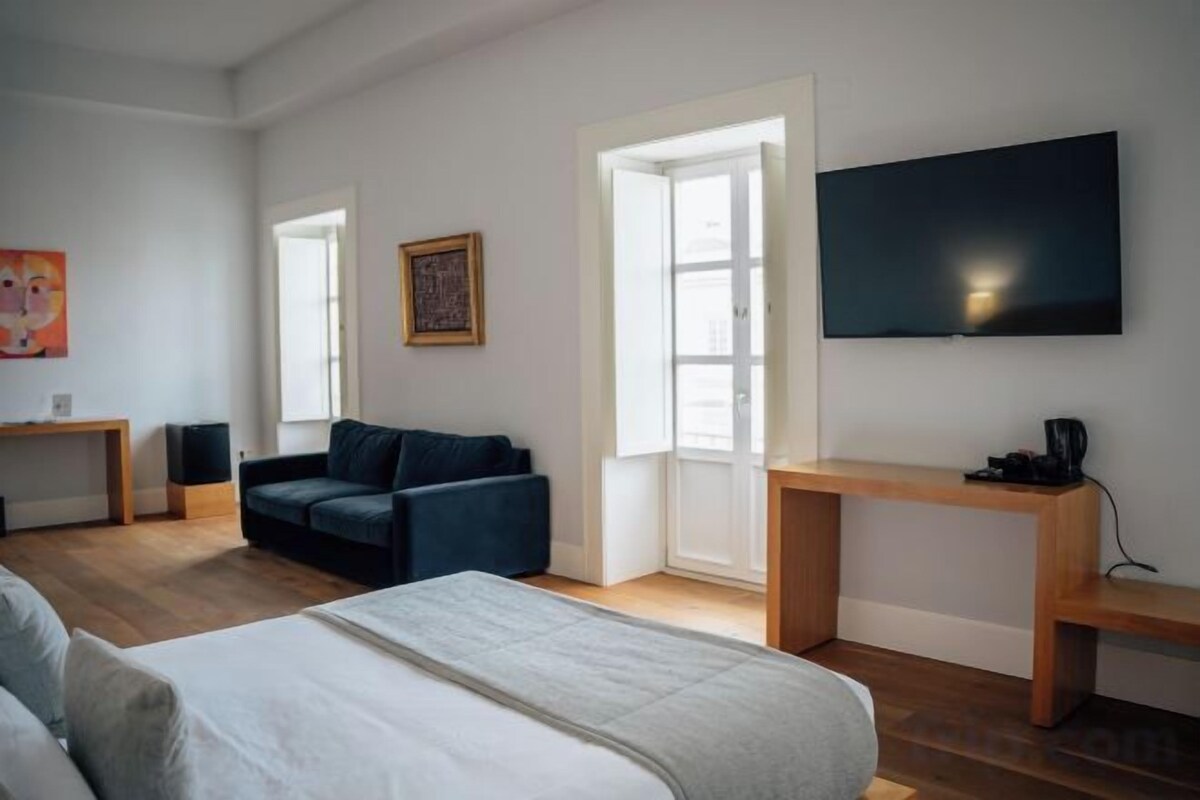 A modern bedroom with a bed, a sofa, a desk, and a TV.