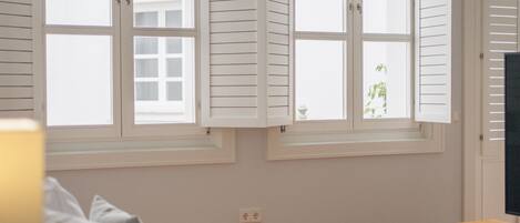 A bedroom with a bed, a nightstand, a lamp, and a window with shutters.