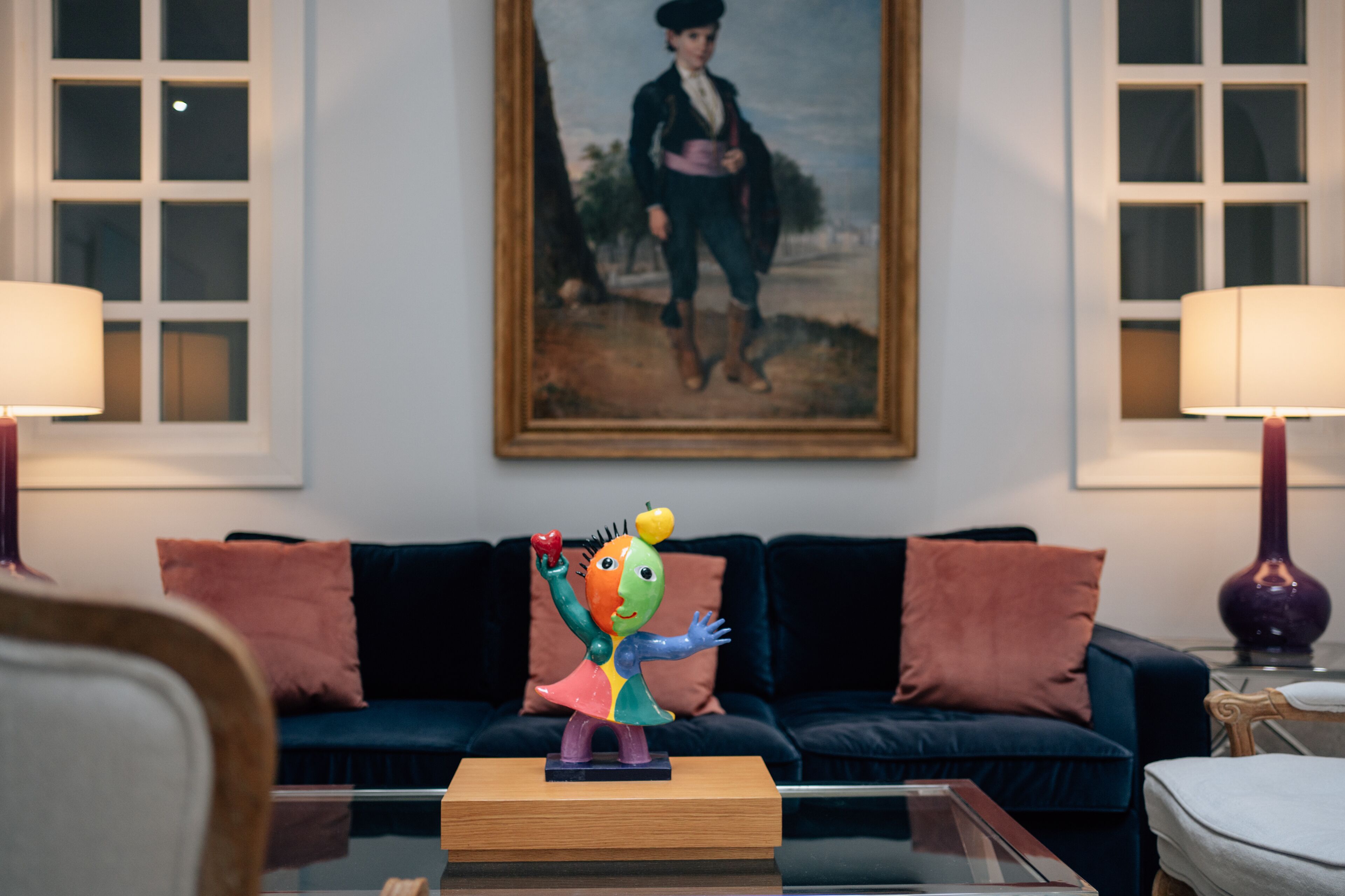 A living room with a dark blue sofa, a colorful sculpture on a wooden table, and a framed painting on the wall.