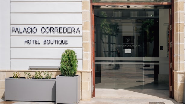 De ingang van Hotel Boutique Palacio Correndera, met een moderne glazen deur en een bord erboven.
