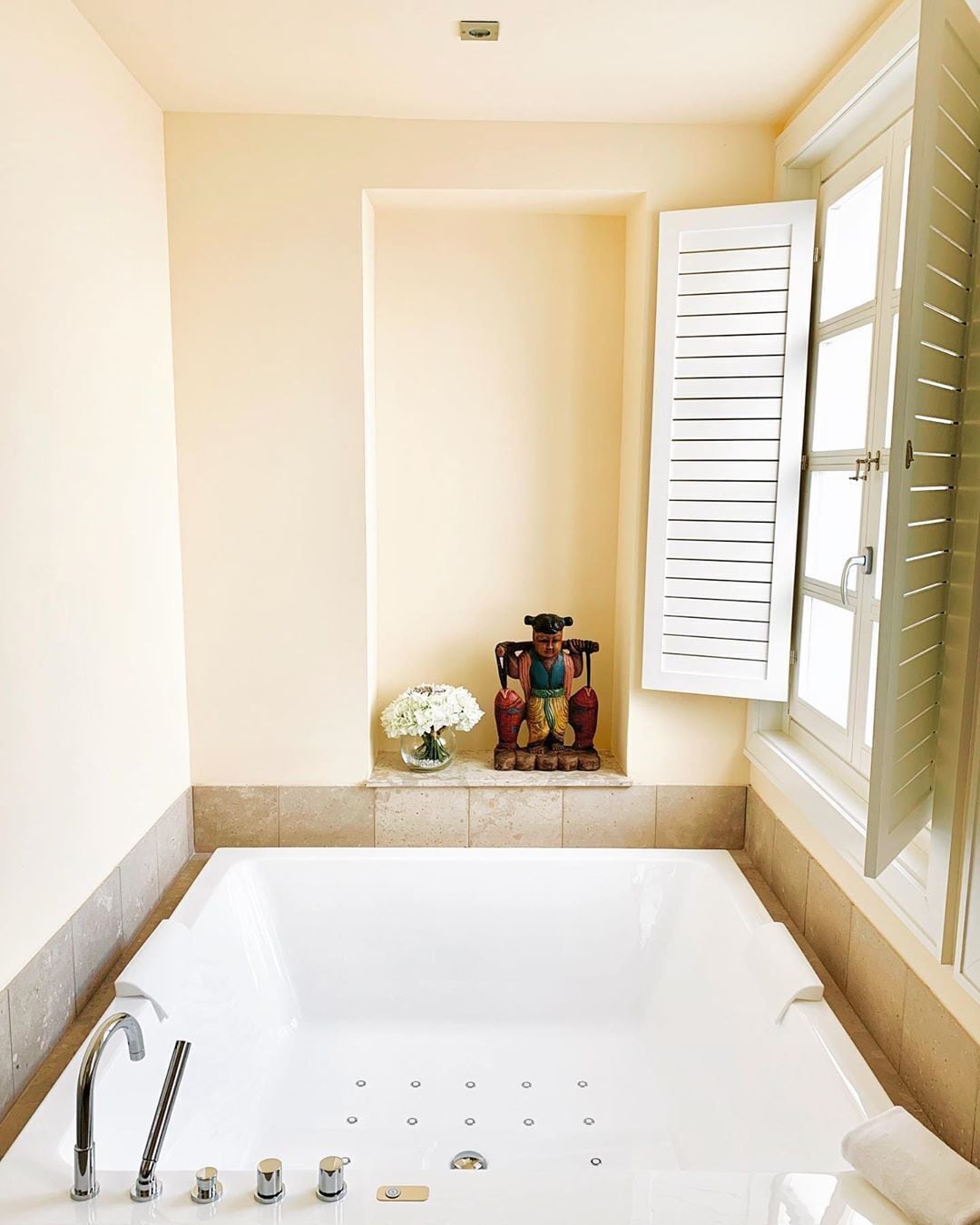 Une salle de bain dotée d’une grande baignoire, d’un espace douche et d’une fenêtre avec des volets.