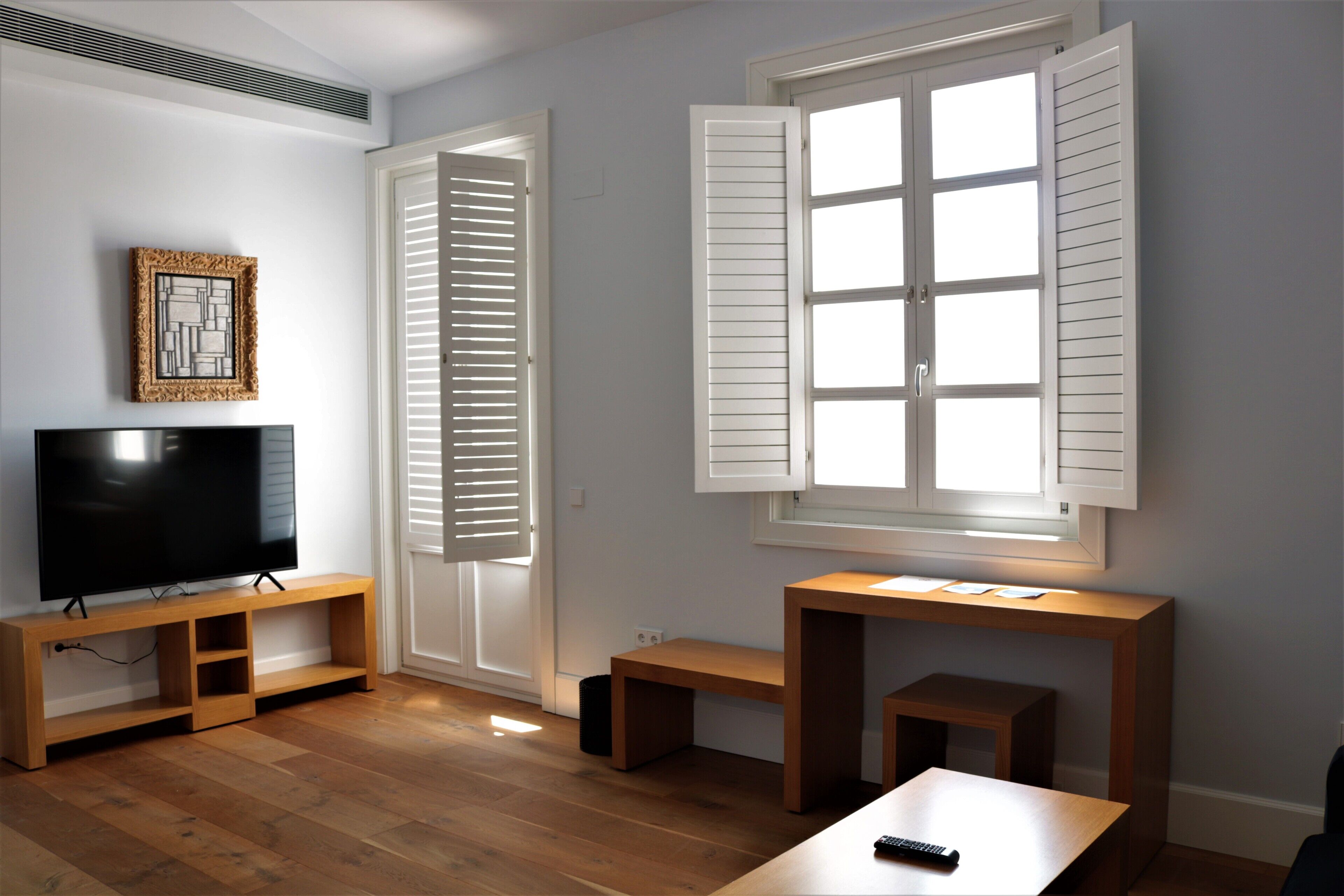 A living room with a flat-screen TV on a wooden stand, a bench, and a table with a remote control.