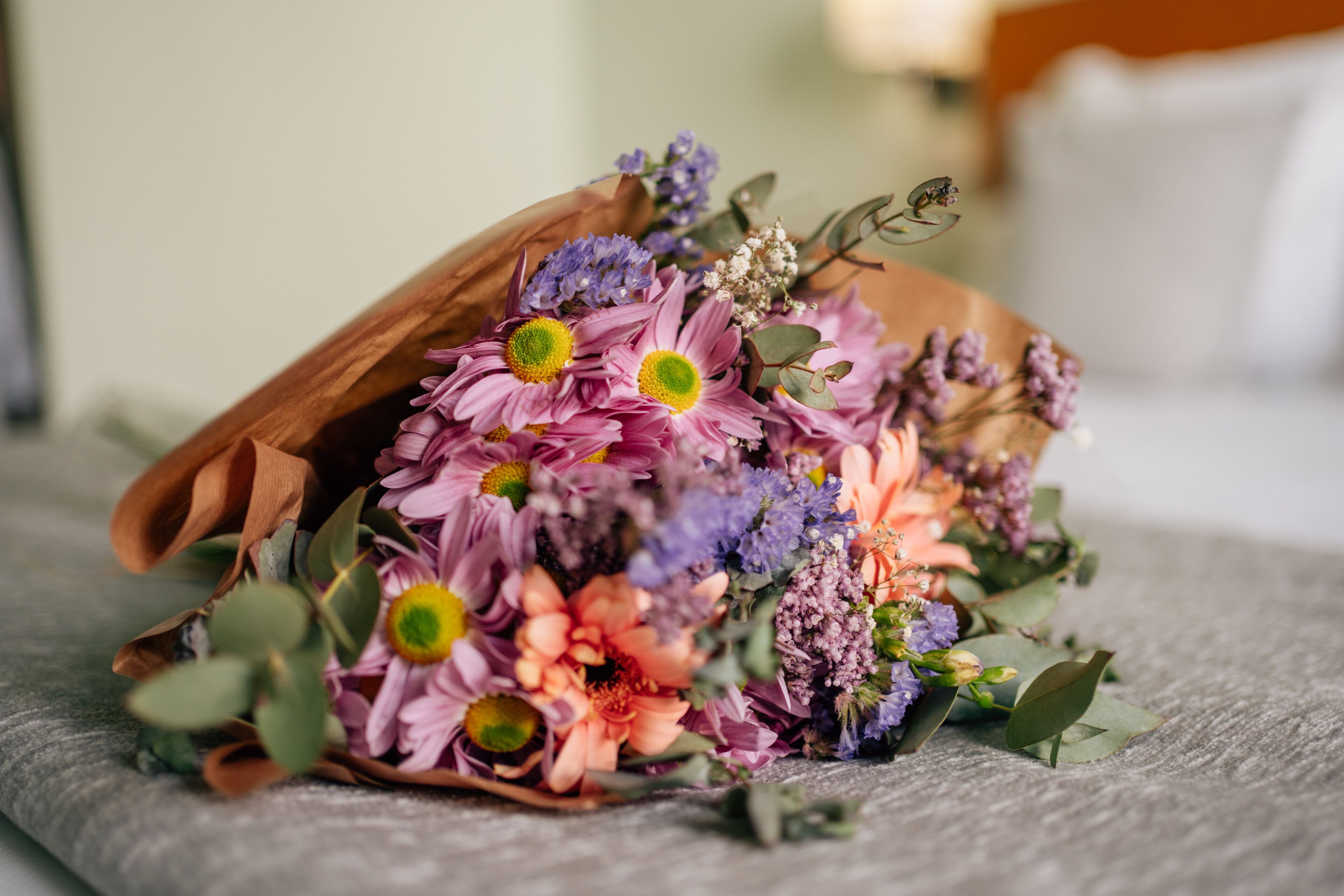 A bouquet of flowers in a brown paper bag on a textured surface.