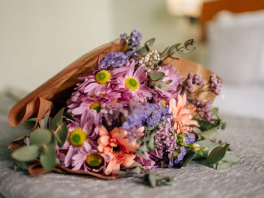 A bouquet of flowers in a brown paper bag on a textured surface.