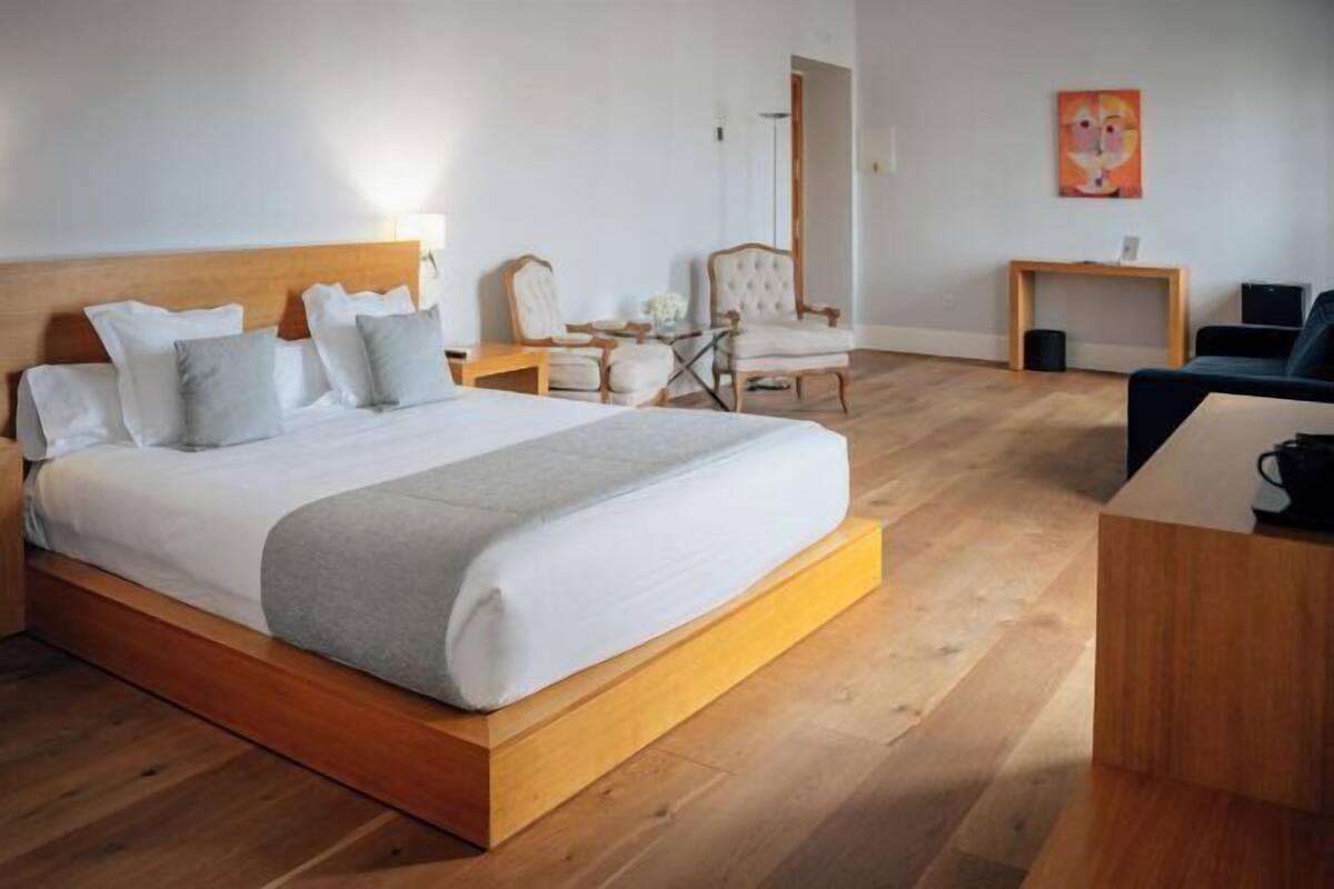 A hotel room with a wooden bed, a small table, a chair, and a desk.