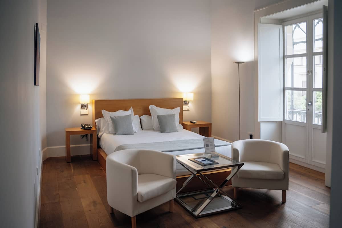 A hotel room with a bed, two bedside tables, a desk with chairs, and a large window.