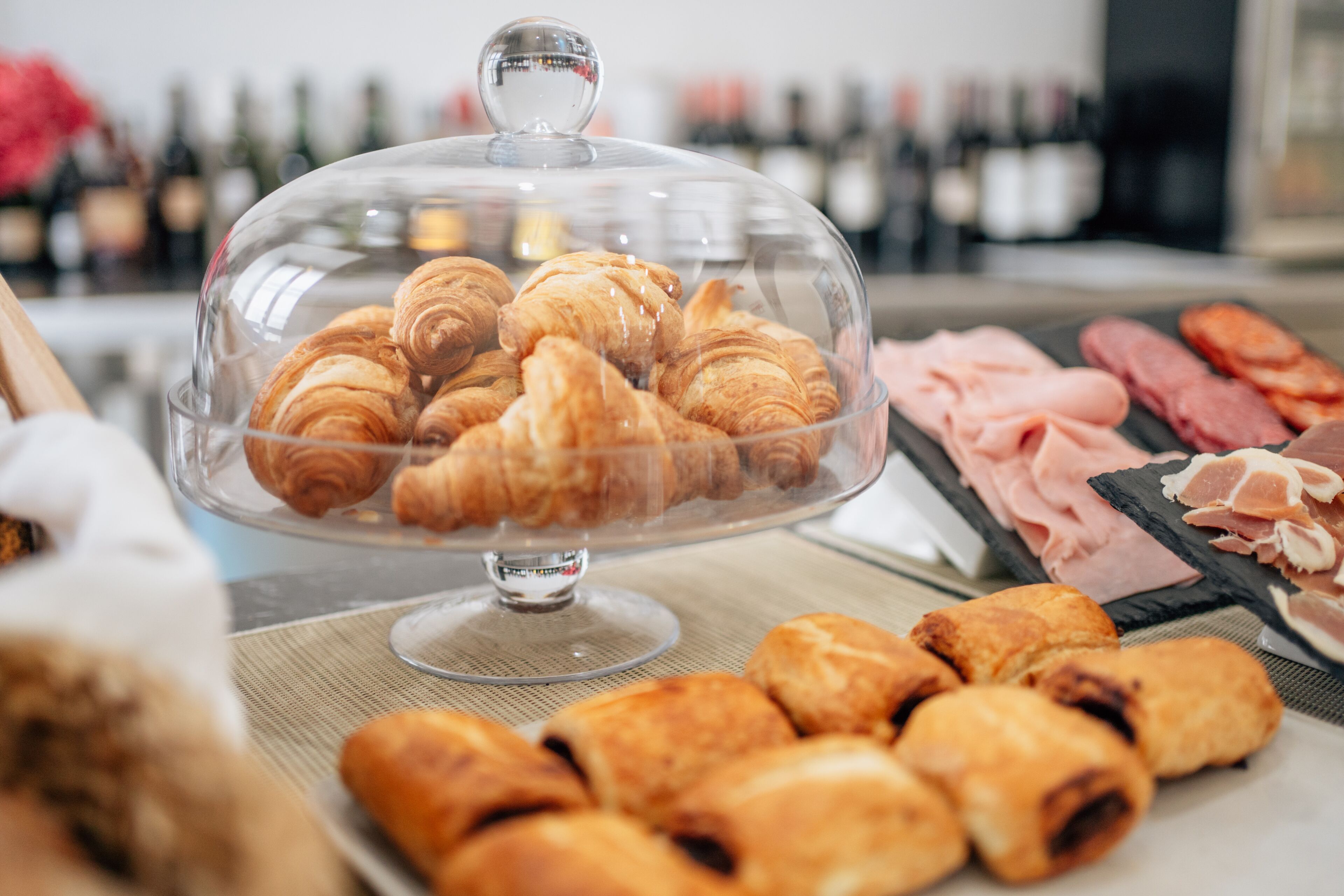 A buffet with a variety of pastries and meats under a glass dome.