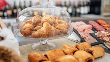 A buffet with a variety of pastries and meats under a glass dome.