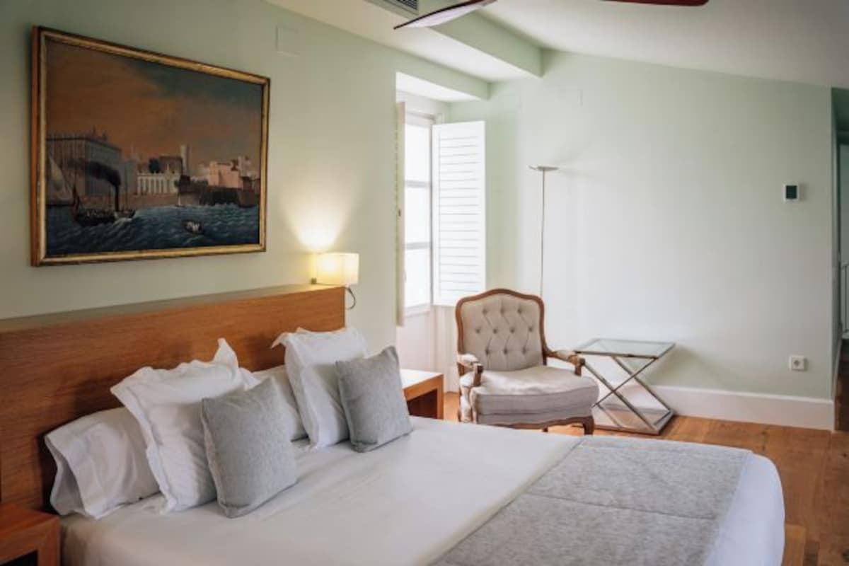 Una habitación de hotel con una cama, una silla, una mesa, un cuadro y una ventana.