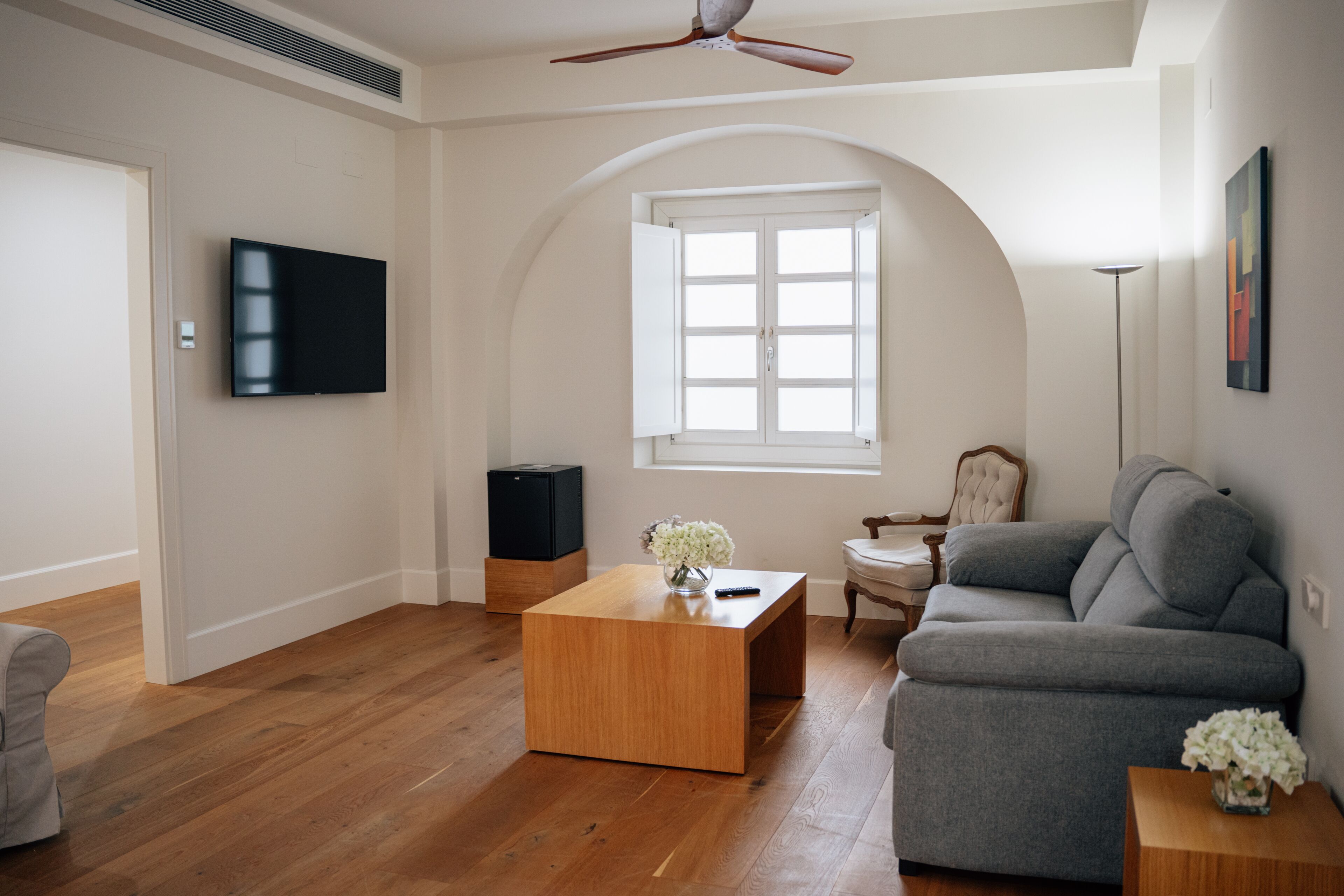 A living room with a wooden coffee table, grey sofa, and a television on the wall.