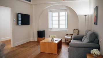 A living room with a wooden coffee table, grey sofa, and a television on the wall.
