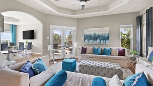 A spacious living room with a ceiling fan, a large painting, and a dining area with chairs and a table.
