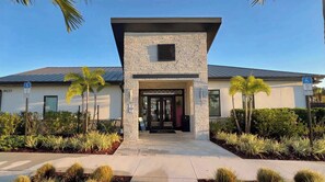 A modern building with a stone facade, a glass entrance, and palm trees in the foreground.