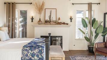 A bedroom with a bed, bench, large plant, fireplace, and windows.