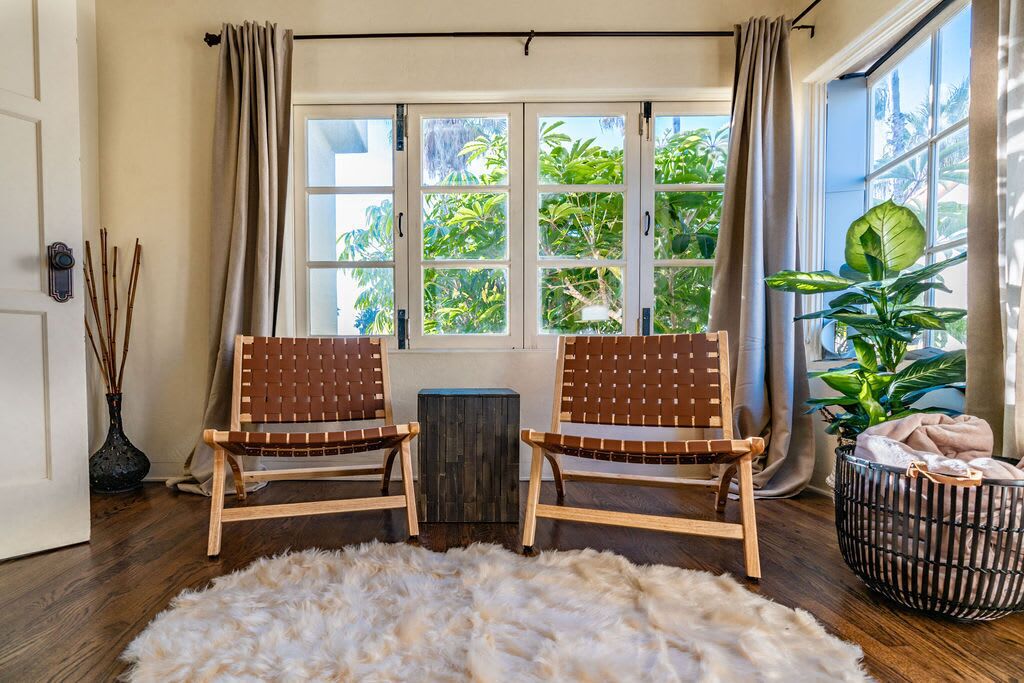 A room with two wooden chairs, a fur rug, a window with curtains, and a plant.