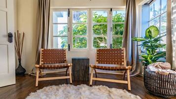 A room with two wooden chairs, a fur rug, a window with curtains, and a plant.