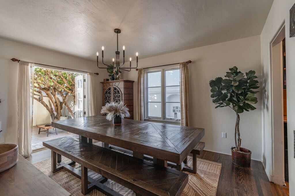 A dining area with a large wooden table, a chandelier, and potted plants.