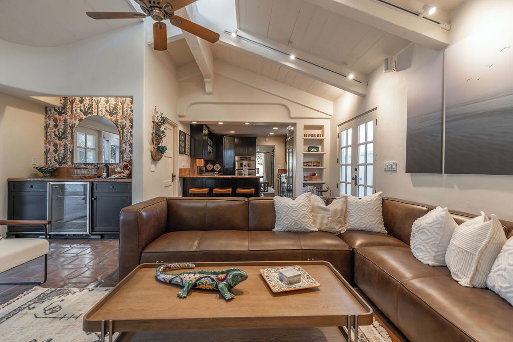 A spacious living room with a brown leather sofa, a wooden coffee table, and a ceiling fan.