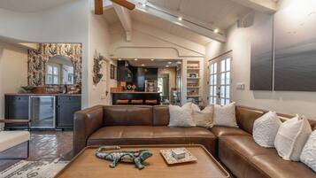 A spacious living room with a brown leather sofa, a wooden coffee table, and a ceiling fan.